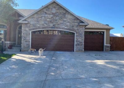 Home with stone facade and new dark stained wooden garage doors. There are two dogs in front